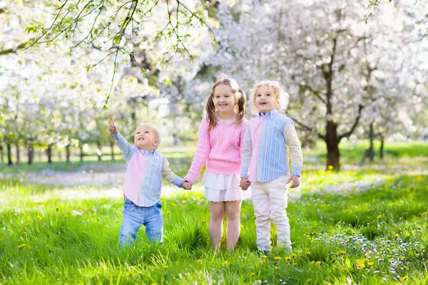 Kinderen op eieren zoeken met Pasen in de bloeiende tuin. — Stockfoto