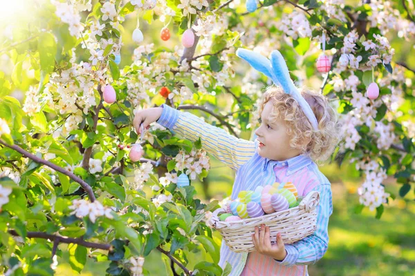 Kinderen op eieren zoeken met Pasen in de bloeiende tuin. — Stockfoto