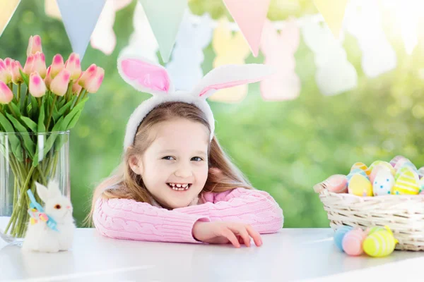滑稽的小女孩在兔子耳朵在复活节早晨在桌与复活节蛋篮子的早餐 孩子们庆祝复活节 儿童复活节彩蛋狩猎 家居装饰 粉彩兔旗和鲜花 — 图库照片