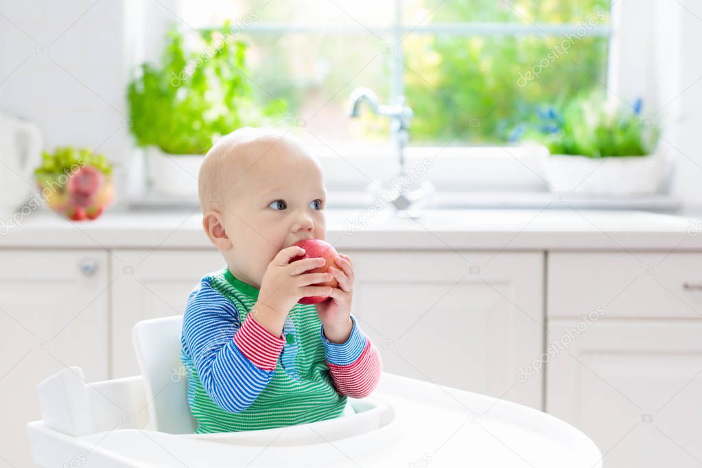 Baby boy eating apple in white kitchen at home