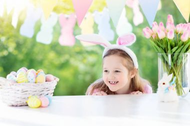 Tavşan kulakları masada Paskalya yumurta sepeti ile Paskalya sabahı kahvaltıda komik küçük kız. Paskalya kutlayan çocuklar. Paskalya yumurtası avı çocuklar. Ev dekorasyon - pastel bunny afiş ve çiçekler.