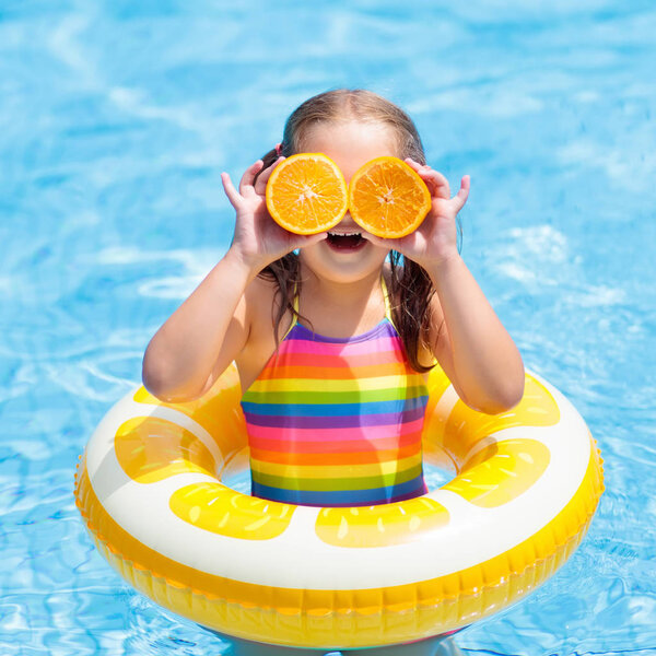 Child in swimming pool. Kid eating orange.