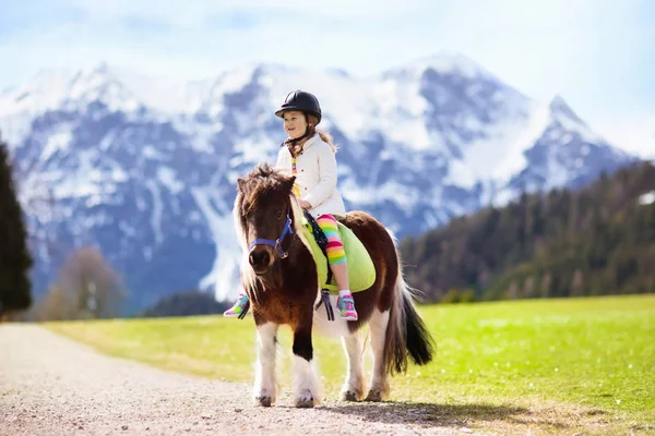 Niños montando pony. Niño a caballo en los Alpes montañas —  Fotos de Stock