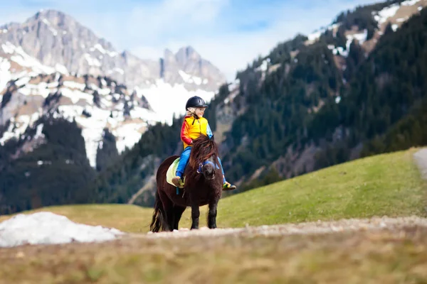 Kids riding pony. Child on horse in Alps mountains