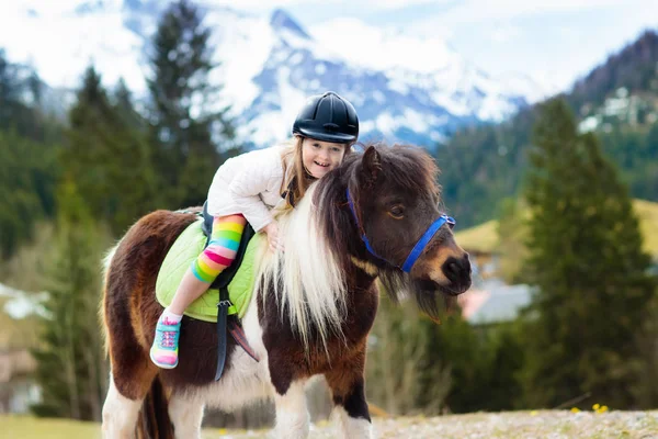 Kids riding pony. Child on horse in Alps mountains