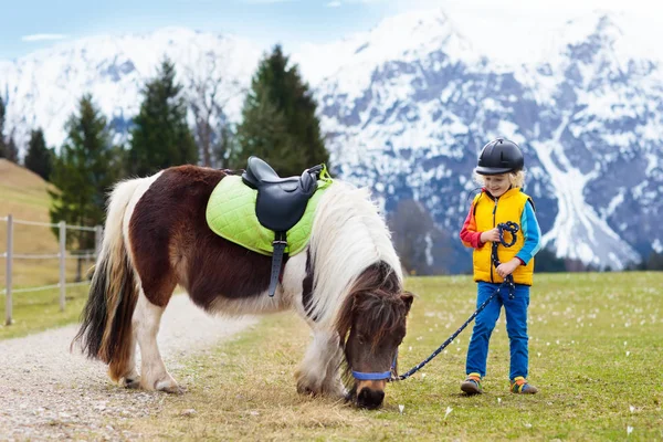 Niños montando pony. Niño a caballo en los Alpes montañas —  Fotos de Stock