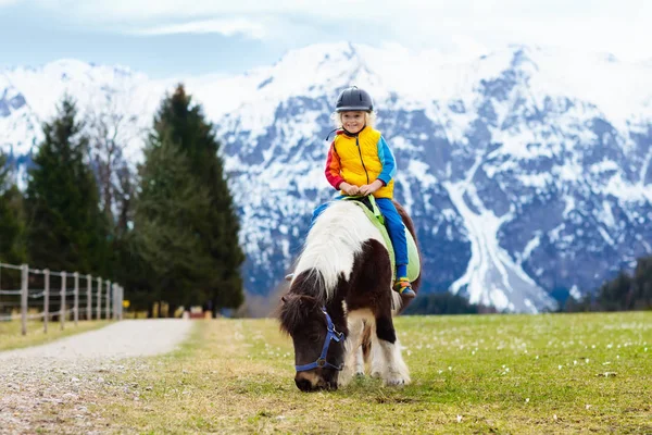 Niños montando pony. Niño a caballo en los Alpes montañas — Foto de Stock