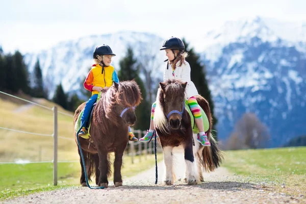 Niños montando pony. Niño a caballo en los Alpes montañas —  Fotos de Stock