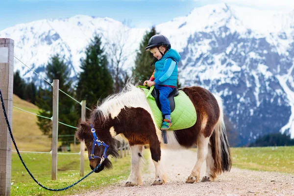 Niños montando pony. Niño a caballo en los Alpes montañas —  Fotos de Stock