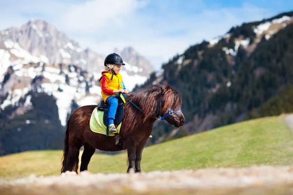 Niños montando pony. Niño a caballo en los Alpes montañas —  Fotos de Stock