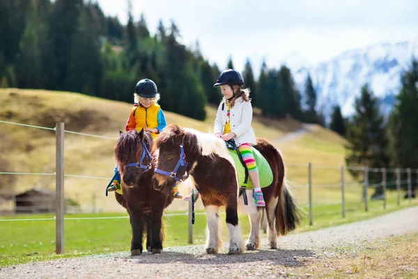 Niños montando pony. Niño a caballo en los Alpes montañas —  Fotos de Stock