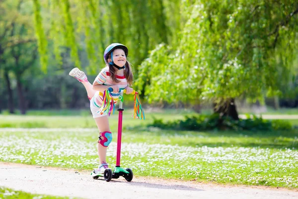 Kind paardrijden kick scooter in zomer park. — Stockfoto