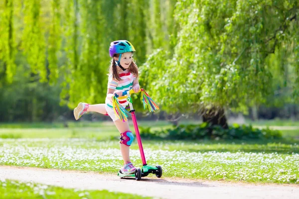 Child riding kick scooter in summer park. — Stock Photo, Image
