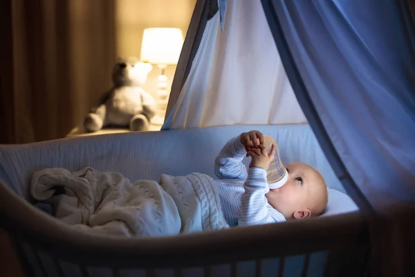 可爱的宝宝喝牛奶在蓝色摇篮与冠层在晚上 小男孩穿着睡衣 公式瓶准备睡在黑暗的房间里 与婴儿床 灯和玩具熊 孩子们的床上时间喝 — 图库照片