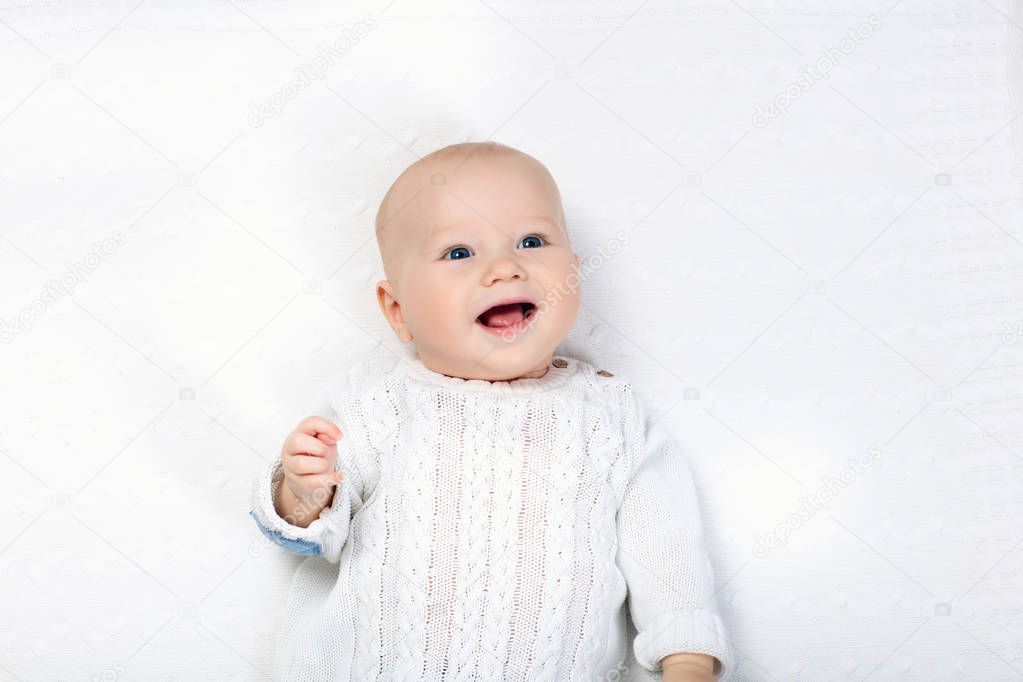 Adorable baby boy in white sunny bedroom. Newborn child relaxing in bed. Nursery for young children. Textile and bedding for kids. Family morning at home. New born kid in knitted sweater.