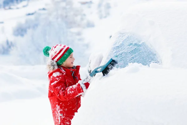 Niño limpiando el coche. Niño con cepillo de nieve de invierno —  Fotos de Stock