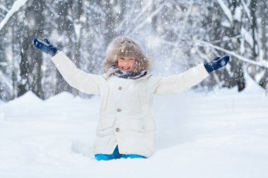 Child playing with snow in winter. Little boy in warm jacket and knitted hat catching snowflakes in winter park on Christmas. Kids play in snowy forest. Cold weather outdoor fun for children.