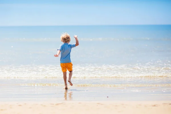 熱帯のビーチで遊んでいる子供たち 子供たちは夏休みに海で泳いだり遊んだりします 砂と水の楽しさ 幼い子供のための太陽の保護 海の岸を走って飛び跳ねる少年 — ストック写真