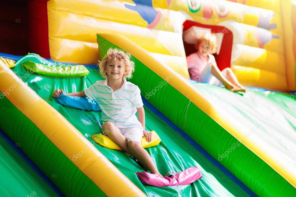 Child jumping on colorful playground trampoline. Kids jump in inflatable bounce castle on kindergarten birthday party Activity and play center for young child. Little boy playing outdoors in summer.