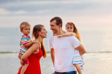 Tropik sahilde çocuklu mutlu bir aile. Deniz tatili. Ebeveynler ve çocuklar gün batımında okyanus kıyısında yürüyorlar. Yaz eğlencesi. Bebek ve küçük çocukla seyahat et. Anne, baba, oğul ve kız oynuyor..
