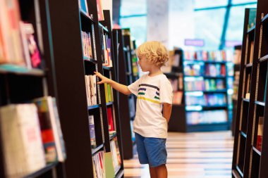 Okul kütüphanesindeki çocuk. Çocuklar kitap okur. Küçük çocuk okuyor ve çalışıyor. Kitapçıdaki çocuklar. Akıllı akıllı anaokulu çocuğu ödünç kitap seçiyor..