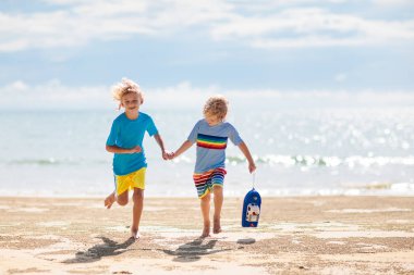 Tropik plajda oynayan çocuklar. Çocuklar yaz tatilinde yüzer ve denizde oynarlar. Kum ve su eğlencesi, küçük çocuklar için güneş koruması. Okyanus kıyısında koşan ve zıplayan küçük çocuk.