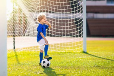 Çocuklar stadyum sahasında futbol oynarlar. Çocuklar futbol maçında gol atıyor. Küçük çocuk topa vuruyor. Okul spor kulübü. Genç oyuncu için alıştırma.