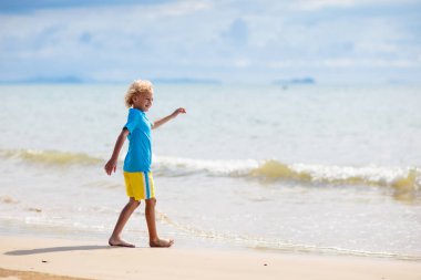 Tropik plajda oynayan çocuklar. Çocuklar yaz tatilinde yüzer ve denizde oynarlar. Kum ve su eğlencesi, küçük çocuklar için güneş koruması. Okyanus kıyısında koşan ve zıplayan küçük çocuk.