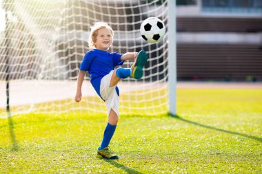Çocuklar stadyum sahasında futbol oynarlar. Çocuklar futbol maçında gol atıyor. Küçük çocuk topa vuruyor. Okul spor kulübü. Genç oyuncu için alıştırma.