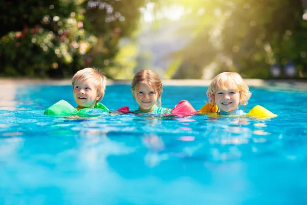 子供たちは熱帯リゾートの屋外スイミングプールで遊びます 幼い子供のための水泳援助 飛び込むことを学ぶ赤ん坊 水で遊んでいる子供たちのグループ カラフルなライフジャケット ビーチと夏の楽しみ — ストック写真