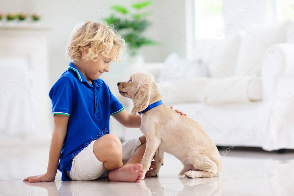 Child playing with baby dog. Kids play with puppy. Little boy and American cocker spaniel at couch at home. Children and pets at home. Kid sitting on the floor with pet. Animal care.