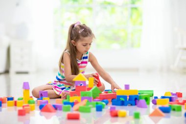 Kids play with colorful blocks. Little girl building tower at home or day care. Educational toy for young child. Construction creative game for baby or toddler kid. Mess in kindergarten playroom.