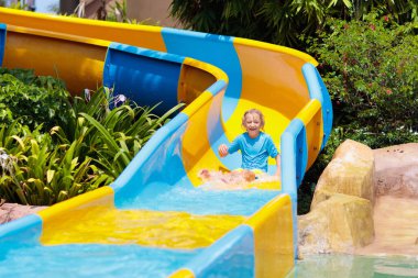 Su parkında su kayağı yapan çocuklar. Çocuklar yaz tatilinde tropik tatil köylerinde su kaydırağında eğleniyorlar. Islak çocuk ve bebek parkı olan eğlence parkı.