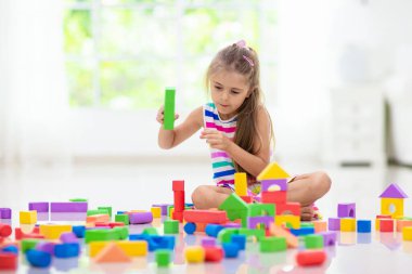 Kids play with colorful blocks. Little girl building tower at home or day care. Educational toy for young child. Construction creative game for baby or toddler kid. Mess in kindergarten playroom.