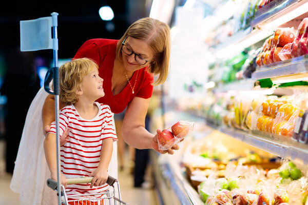 Shopping with kids. Mother and child buying fruit in supermarket. Mom and little boy buy fresh mango in grocery store. Family in shop. Parent and children in a mall choosing vegetables. Healthy food.