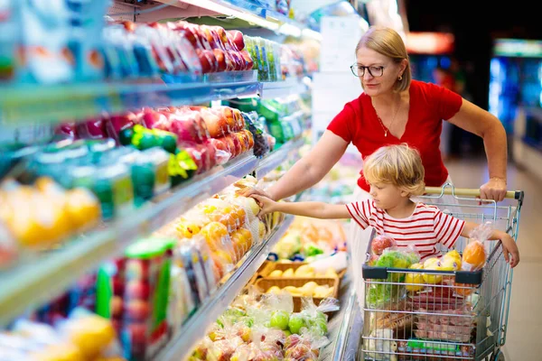 Shopping with kids. Mother and child buying fruit in supermarket. Mom and little boy buy fresh mango in grocery store. Family in shop. Parent and children in a mall choosing vegetables. Healthy food.