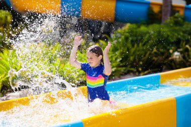 Su parkında su kayağı yapan çocuklar. Çocuklar yaz tatilinde tropik tatil köylerinde su kaydırağında eğleniyorlar. Islak çocuk ve bebek parkı olan eğlence parkı.