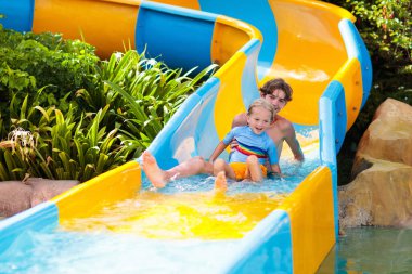 Su parkında su kayağı yapan çocuklar. Çocuklar yaz tatilinde tropik tatil köylerinde su kaydırağında eğleniyorlar. Islak çocuk ve bebek parkı olan eğlence parkı.