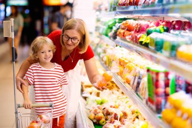 Shopping with kids. Mother and child buying fruit in supermarket. Mom and little boy buy fresh mango in grocery store. Family in shop. Parent and children in a mall choosing vegetables. Healthy food.