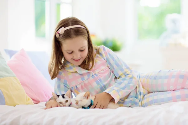 孩子们在白色卧室的床上和小猫咪玩耍 抱着白猫的小孩小女孩穿着睡衣 家里有可爱的宠物动物 孩子们和猫玩耍 儿童和家畜宠物 — 图库照片