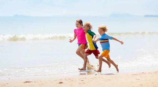 熱帯のビーチで遊んでいる子供たち 子供たちは夏休みに海で泳いだり遊んだりします 砂と水の楽しさ 幼い子供のための太陽の保護 海の岸を走って飛び跳ねる少年 — ストック写真