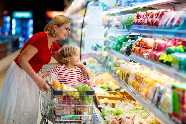 Shopping with kids. Mother and child buying fruit in supermarket. Mom and little boy buy fresh mango in grocery store. Family in shop. Parent and children in a mall choosing vegetables. Healthy food.