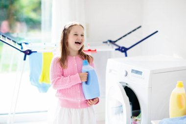 Çocuk Çamaşırhane, çamaşır makinesi ile Oda veya kurutma. Çocuk ile aile işleri yardımcı. Modern ev aygıtları ve çamaşır deterjan beyaz güneşli evinde. Raf kurutma üzerinde temiz yıkanmış kıyafetler. 