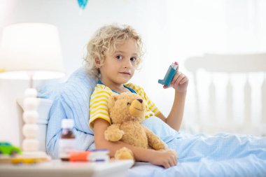 Astım ilacıyla hasta küçük bir çocuk. Hasta çocuk yatakta yatıyor. Öksürük tedavisi için spreyi olan hasta bir çocuk. Grip mevsimi. Genç hastalar için yatak odası ya da hastane odası. Sağlık ve İlaç Hizmetleri.