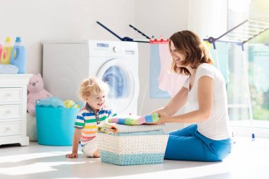 Anne ve çocuklar Çamaşırhane, çamaşır makinesi ile Oda veya kurutma. Aile işleri. Modern ev aygıtları ve çamaşır deterjan beyaz güneşli evinde. Raf kurutma üzerinde temiz yıkanmış kıyafetler. 
