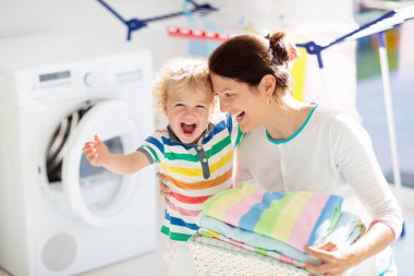Anne ve çocuklar Çamaşırhane, çamaşır makinesi ile Oda veya kurutma. Aile işleri. Modern ev aygıtları ve çamaşır deterjan beyaz güneşli evinde. Raf kurutma üzerinde temiz yıkanmış kıyafetler. 