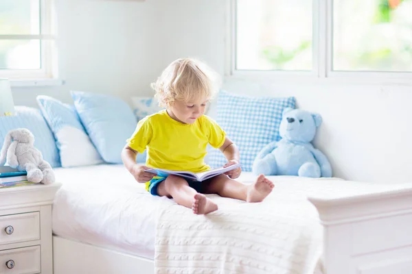 子供は窓付きの白い日当たりの良いベッドルームでベッドで遊ぶ キッズルームとインテリアデザイン 家にいる赤ん坊 子供の保育園のための寝具と繊維 おもちゃと本を持つ子供 昼寝と睡眠時間 — ストック写真