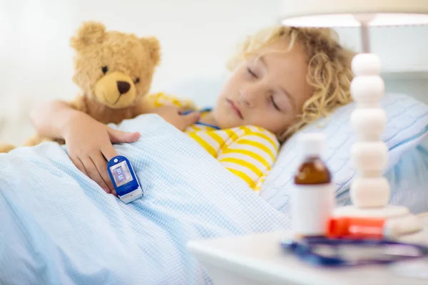 生病的小男孩 手指上戴着脉搏血氧计 哮喘的治疗 生病的孩子躺在床上 有卧房吸入器的病童咳嗽药流感季节 年轻病人的卧房或医院房间 — 图库照片