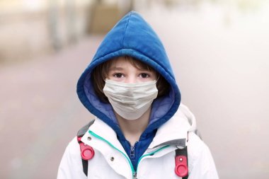 Virüs salgını sırasında okula giden maskeli çocuk. Coronavirus karantina ve tecrit. Cerrahi koruyucu maskeli küçük bir çocuk. Grip ya da hava kirliliğine karşı koruyucu giysi giyen bir öğrenci. Çocukların güvenliği