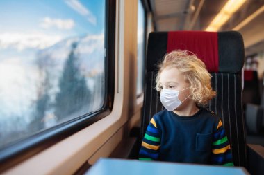 Trendeki çocuk maske takıyor. Virüs salgını. Coronavirus ve grip salgını. Küçük çocuk ve bebekle iyi yolculuklar. Küçük çocuk, cerrahi maske takarak vagonun yolcu vagonunda oturuyor..
